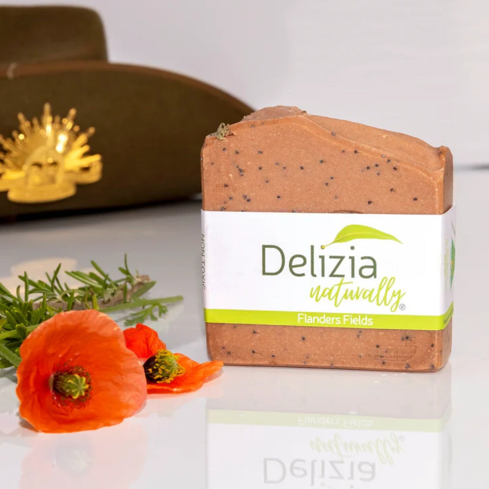 Bar of Flanders Fields Remembrance Soap handmade by Delizia Naturally, artfully arranged alongside red poppies, rosemary and an Australian Army slouch hat.