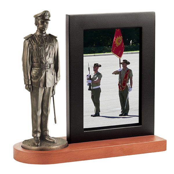 Bronze statue of a military figure on a wooden base with a black frame displaying a photo of two soldiers.